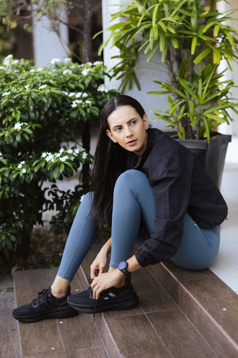Kamila Rodrigues sentada num degrau, amarrando o tênis antes do treino